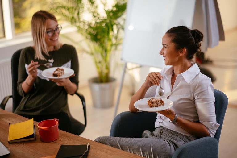 Zwei junge Frauen essen Kuchen im Büro.