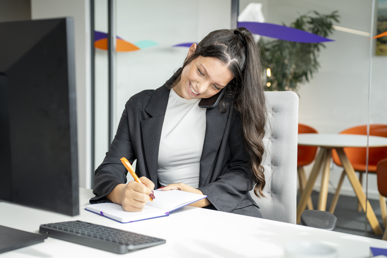 Junge Frau telefoniert im Büro und macht Notizen.