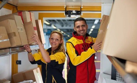 Zwei Paketboten im Postauto bei DHL lächeln in die Kamera