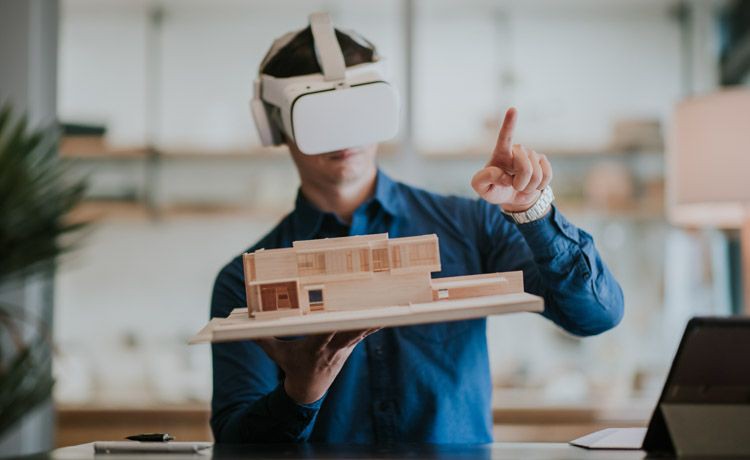 Junger Mann mit VR-Brille hält das Modell eines Gebäudes in den Händen.