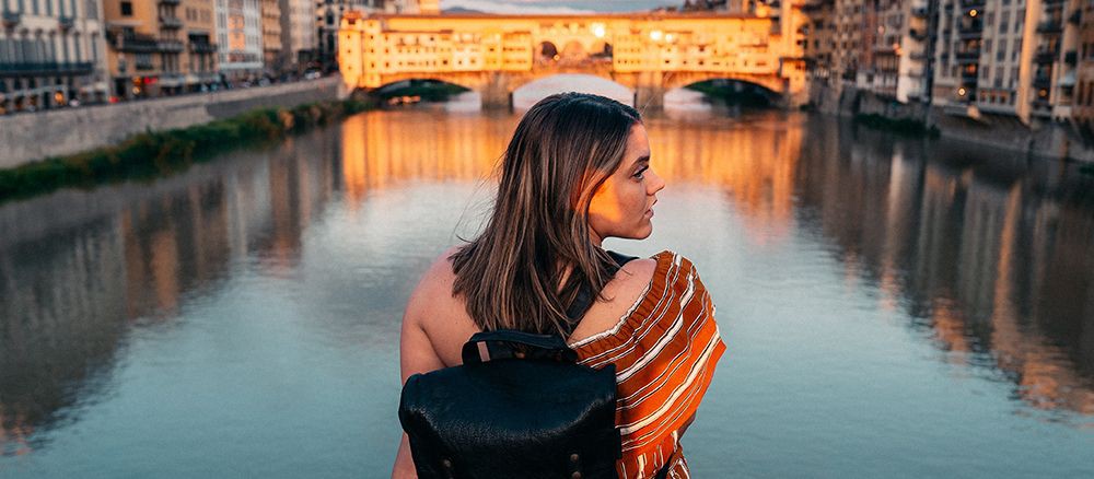 Mädchen sitzt auf einer Brücke in Florenz mit der Ponte Vecchio im Hintergrund