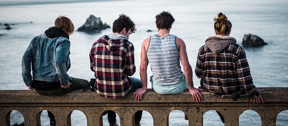 Vier junge Auszubildende sitzen im Ausland auf einer Brüstung mit Blick aufs Meer