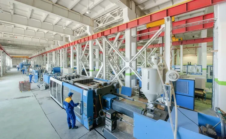 Kunststoff- und Kautschuktechnologe arbeitet in einer großen Halle mit Maschinen.