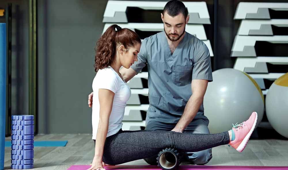 Gymnastiklehrer unterstützt Patientin bei einer Übung.