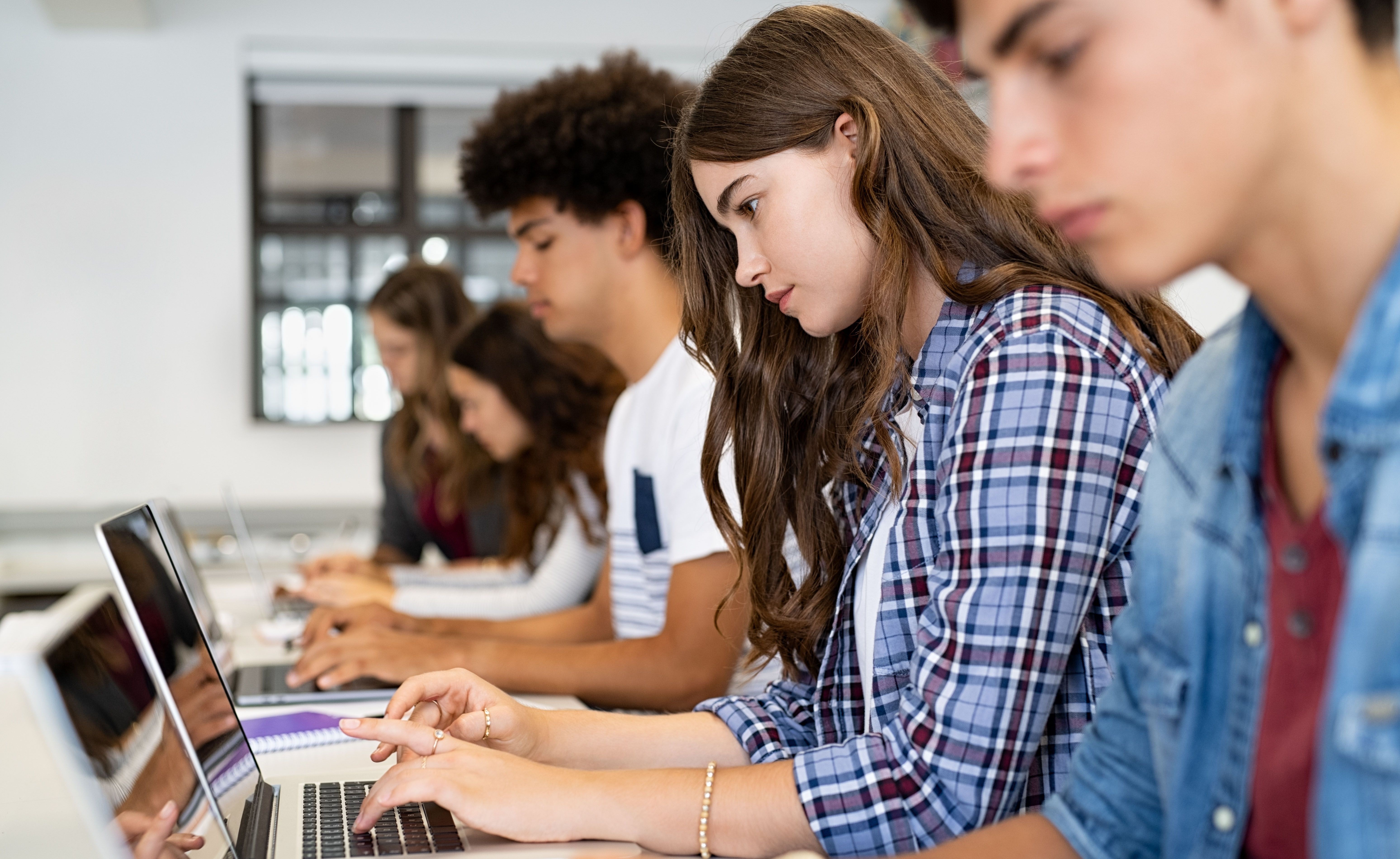 Studierende sitzen in einer Reihe und arbeiten am Laptop.