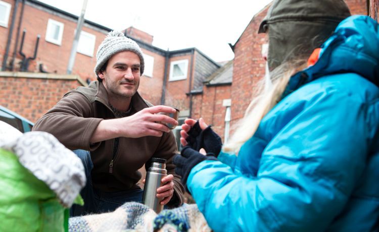 Junger Sozialarbeiter bringt obdachlosem Mann einen warmen Tee.