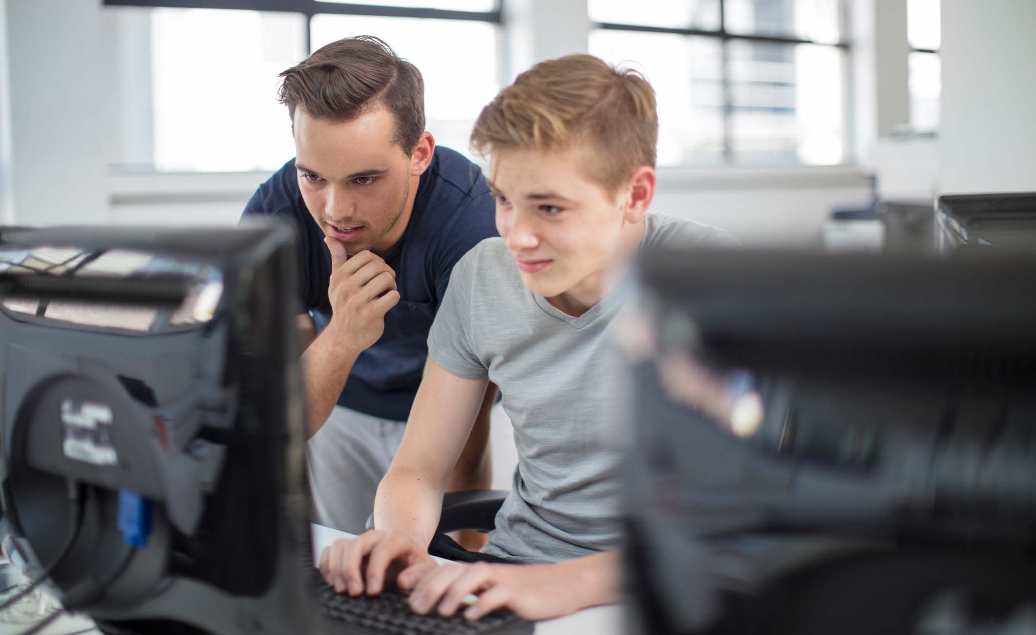 Zwei junge Männer schauen gemeinsam auf den Bildschirm eines PCs