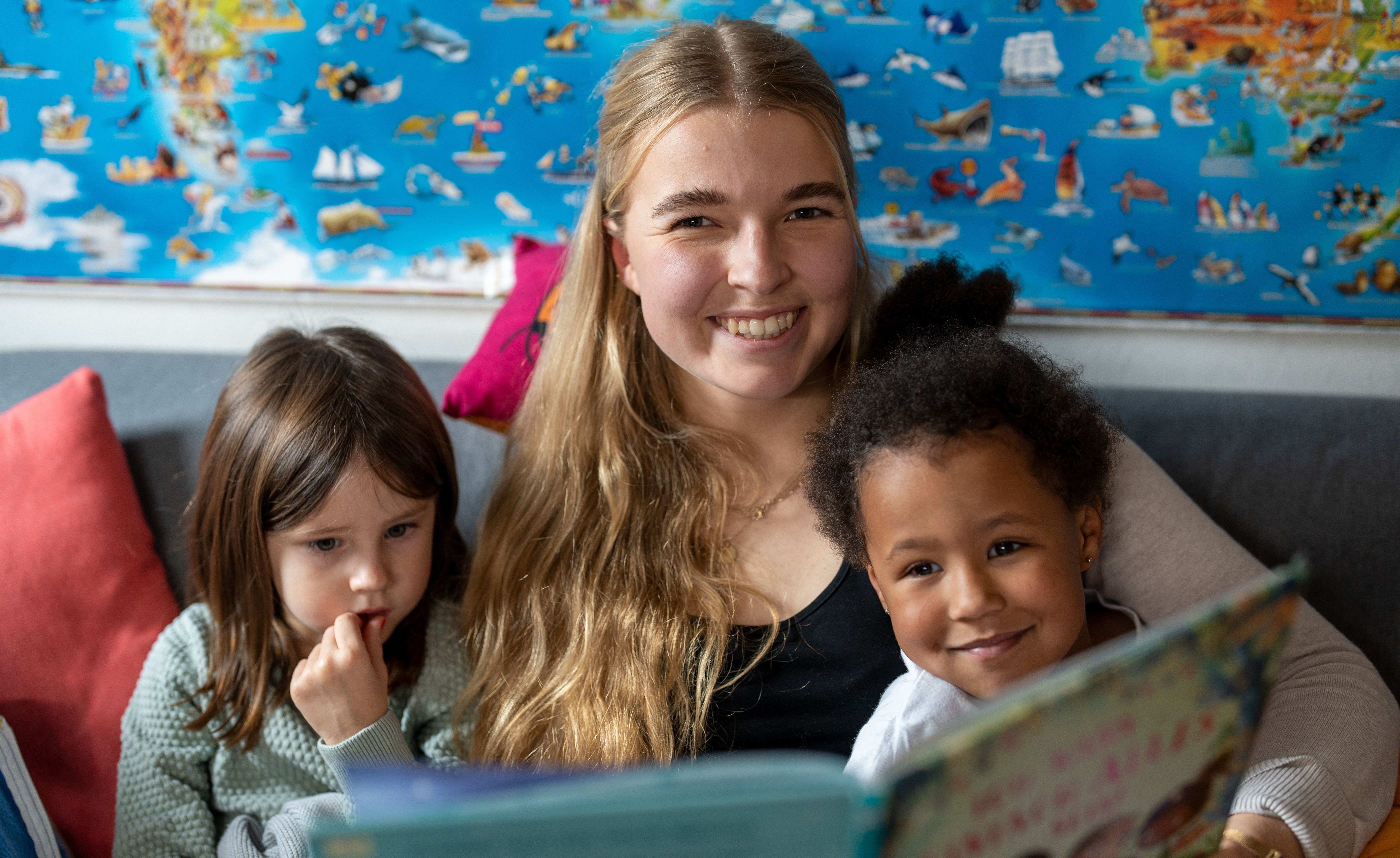 Erzieherin liest zwei Kindern etwas vor.