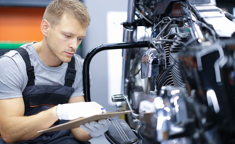 Zweiradmechatroniker inspiziert ein Motorrad.