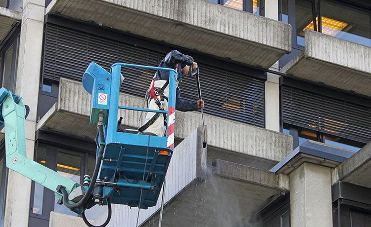 Ein Gebäudereiniger reinigt die Außenwand eines Gebäudes von einer Hebebühne aus
