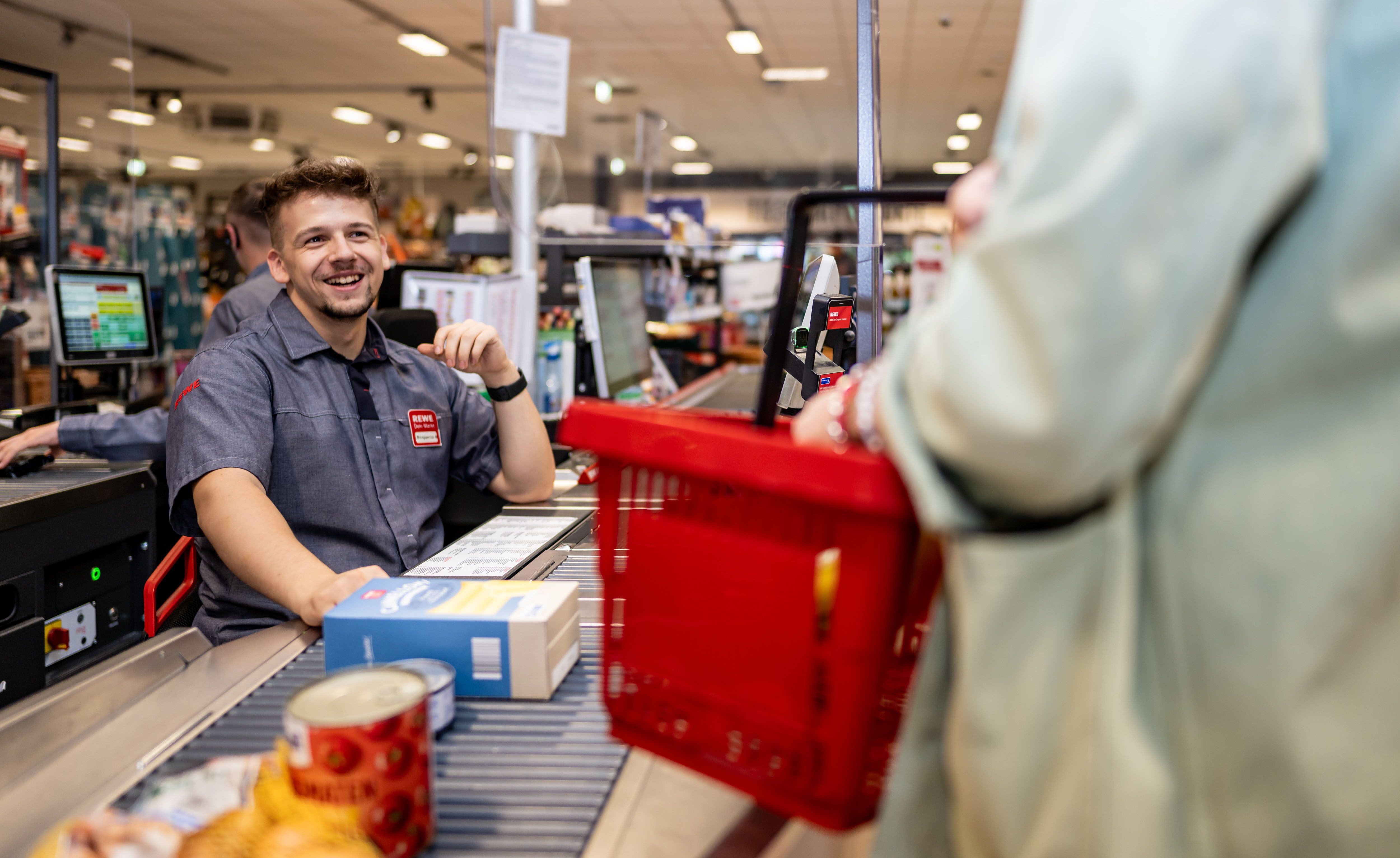 Einzelhandelskaufmann bei REWE an der Kasse.