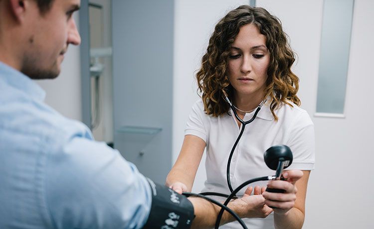 Medizinische Fachangestellte misst Blutdruck bei einem Patienten.