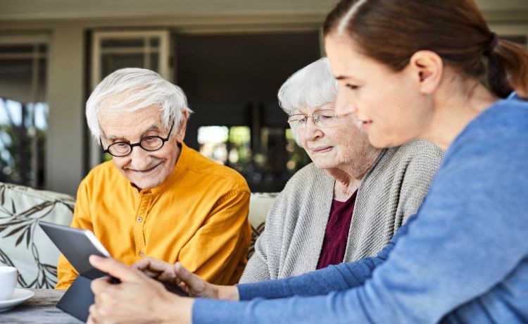 Alltagsbegleiterin zeigt zwei Senioren etwas auf dem iPad.
