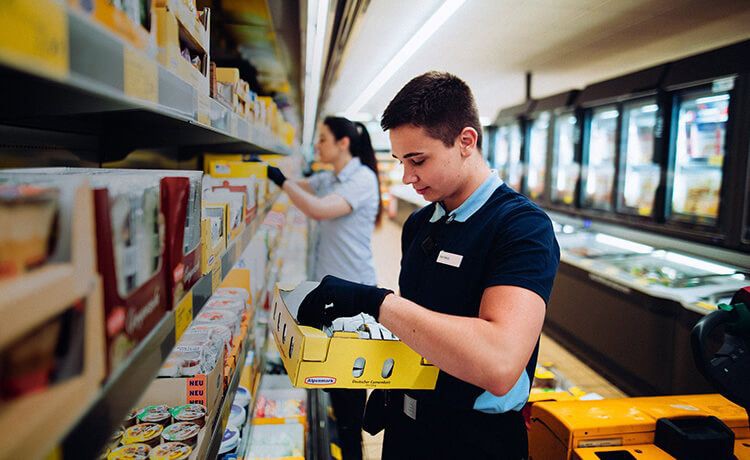 Junger Einzelhandelskaufmann-Azubi räumt Regal im Supermarkt ein..