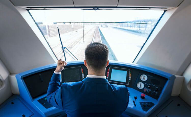 Junger Eisenbahner-Azubi sitzt im Cockpit eines Zugs und blickt auf die Schienen.