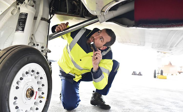 Fluggerätmechaniker kniet unter einem Flugzeug und prüft mit einer Taschenlampe.