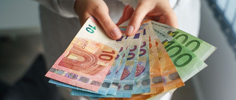 Frau hält mehrere Euro-Geldscheine aufgefächert in der Hand.