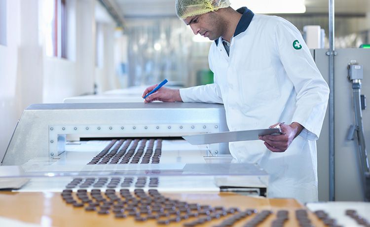 Ein Mann kontrolliert in einer Fabrik die Schokolade auf den Fließbändern.