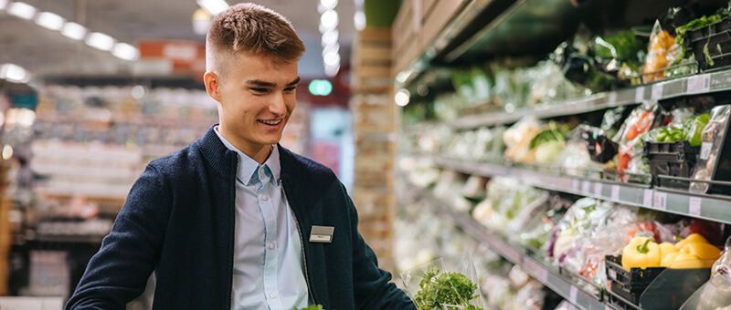 Junger Auszubildender Kaufmann im Einzelhandel räumt ein Regal im Supermarkt ein.