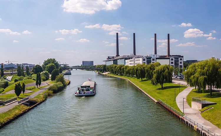 Frachtschiff fährt auf Wasserstraße an einer Fabrik in Wolfsburg vorbei.