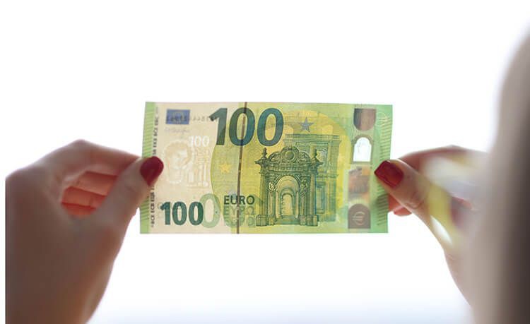 Frau hält 100-Euro-Schein zwischen ihren Fingern und prüft diesen auf Echtheit.