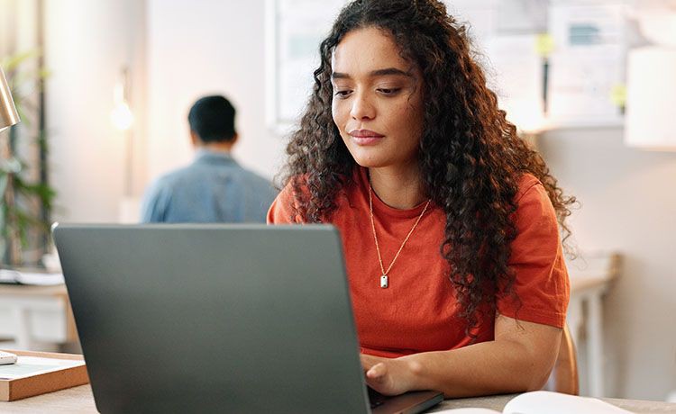 Junge Frau sitzt am Laptop und schreibt einen Text.