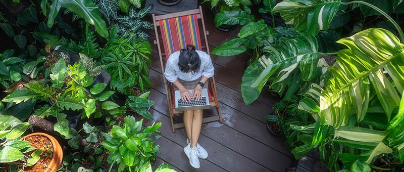 Junges Mädchen sitzt auf einem Liegestuhl im Garten und informiert sich an einem Laptop über duale Ausbildungen.