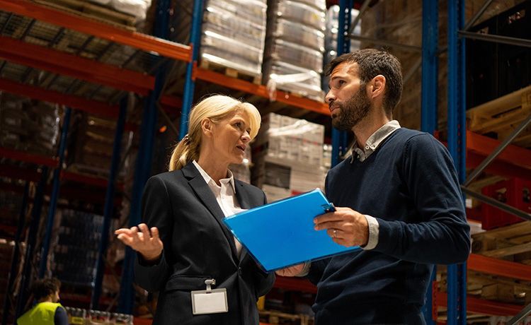 Zwei Logistikmanager unterhalten sich in einer Lagerhalle.