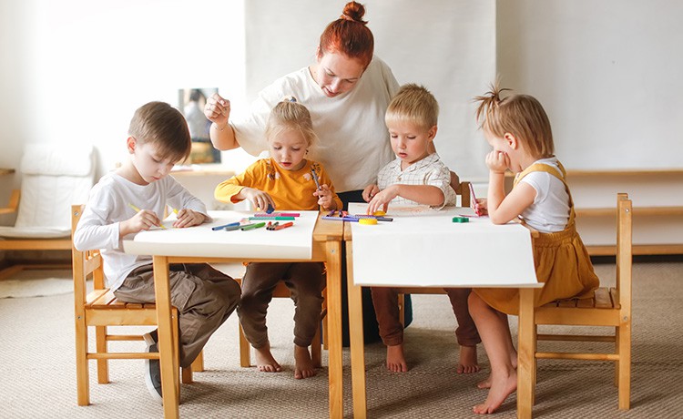 Eine junge Frau sitzt mit ein paar Kindern am Tisch und bastelt.