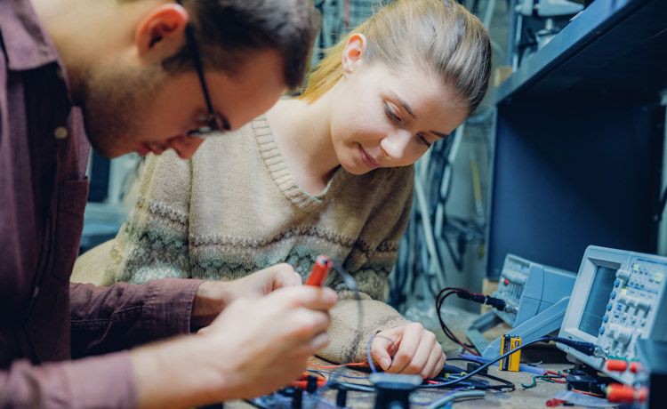 Eine junge Frau und ein junger Mann arbeiten mit elektrischen Anlagen.