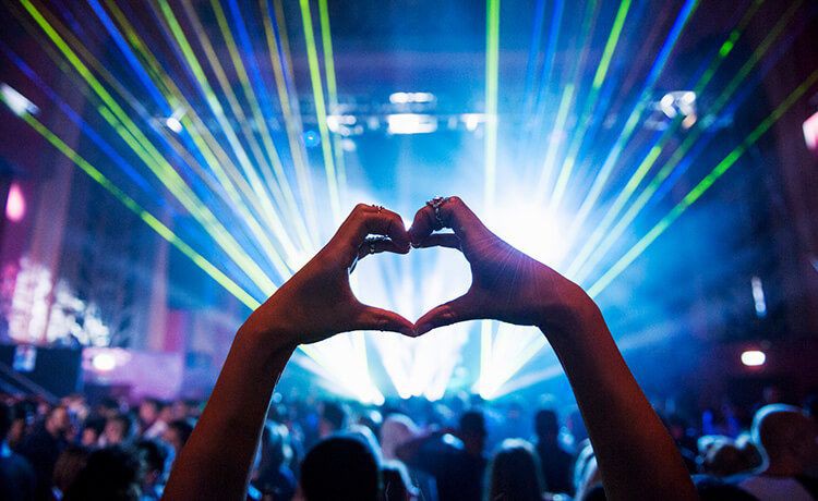 Mit Händen geformtes Herz bei einem Musikevent mit Lasershow.