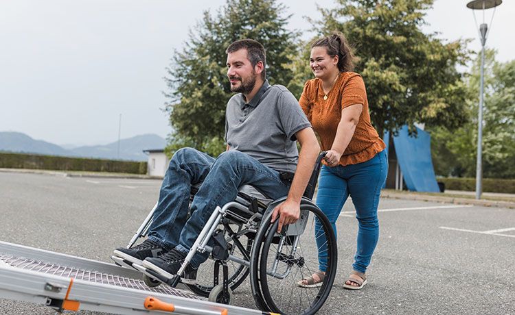 Pflegerin hilft Mann im Rollstuhl ins Auto