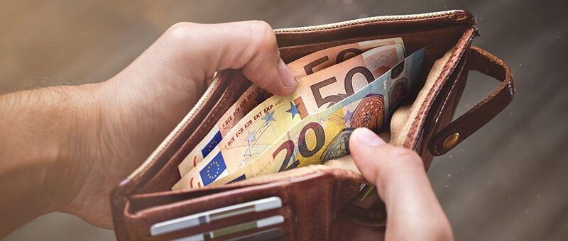 Zwei Hände halten Geldbeutel auf, in dem zwei 50-Euro-Scheine und ein 20-Euro-Schein im Scheinfach liegen.