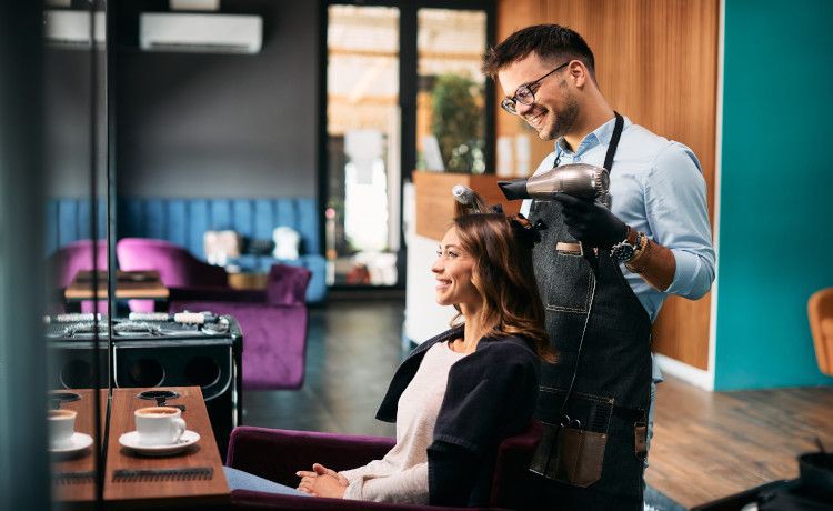 Friseur in der Ausbildung föhnt einer Kundin die Haare.