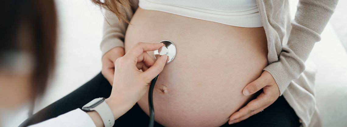Eine Hebamme untersucht den Bauch einer Schwangeren mithilfe eines Stethoskops.