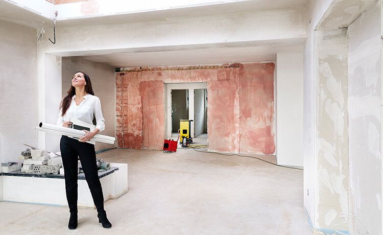 Immobilienkauffrau hält Baupläne in der Hand und schaut sich unrenovierte Wohnung an.