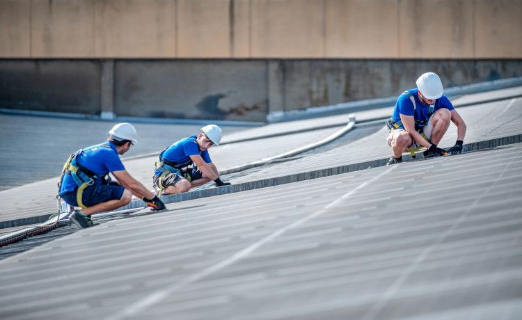 Drei Männer arbeiten auf einem Dach an Solaranlagen.