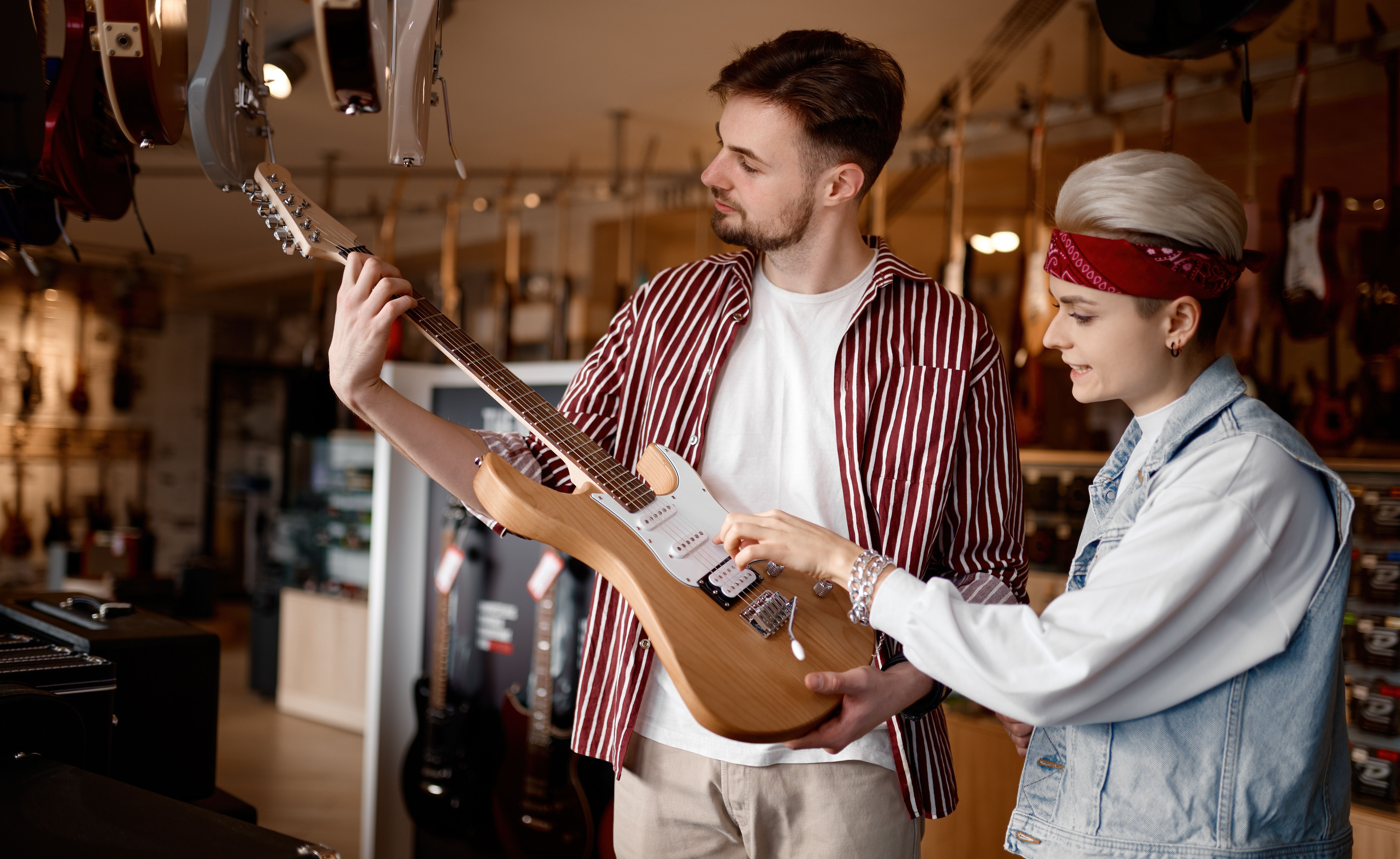 Hipster-Paar sucht in einem professionellen Fachgeschäft nach einer neuen E-Gitarre für Auftritte und wählt ein Saiteninstrument aus.