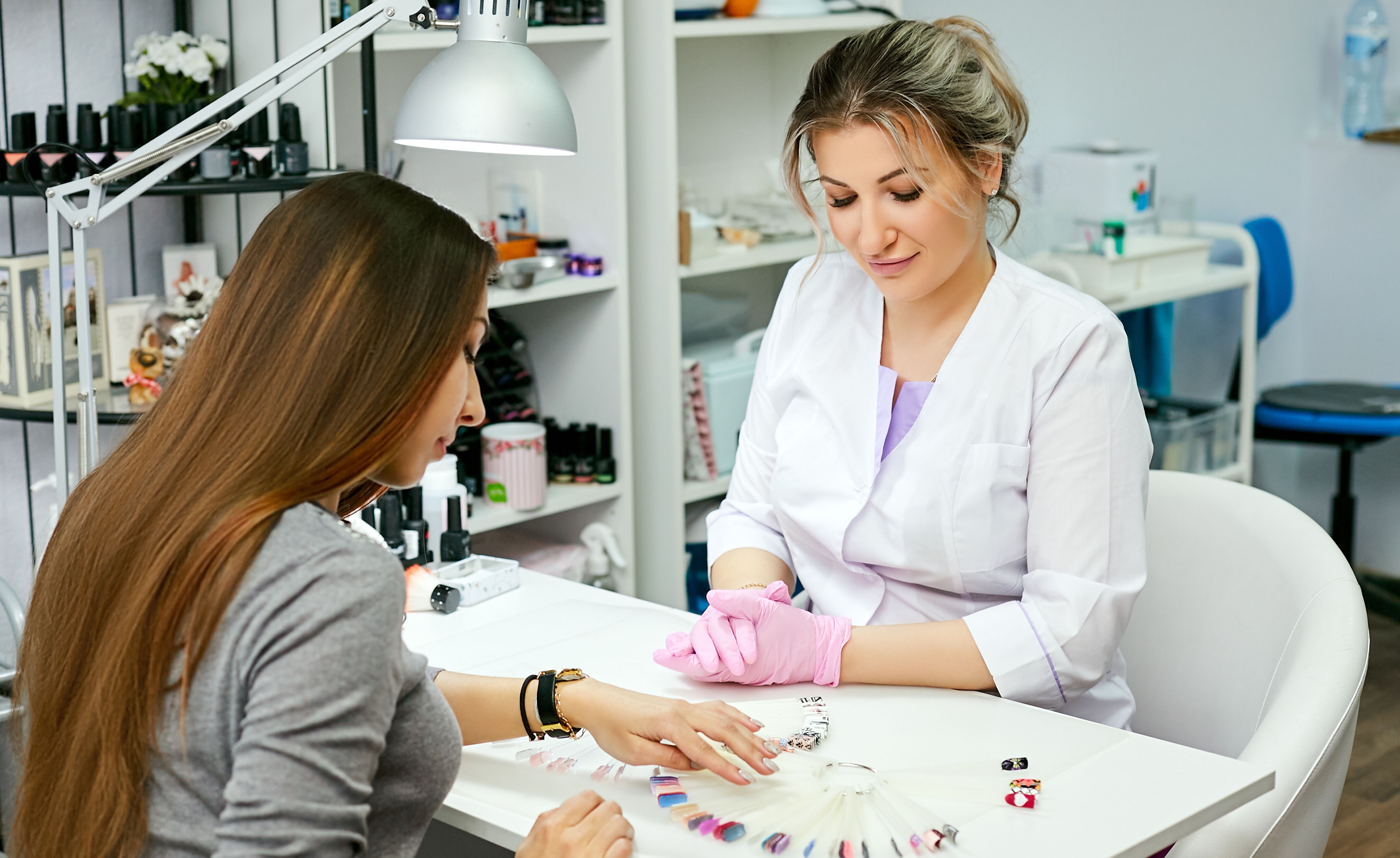 Eine Nageldesignerin hilft dabei, im Salon das passende Design und die passende Farbe für die Nägel der Kundin auszuwählen.