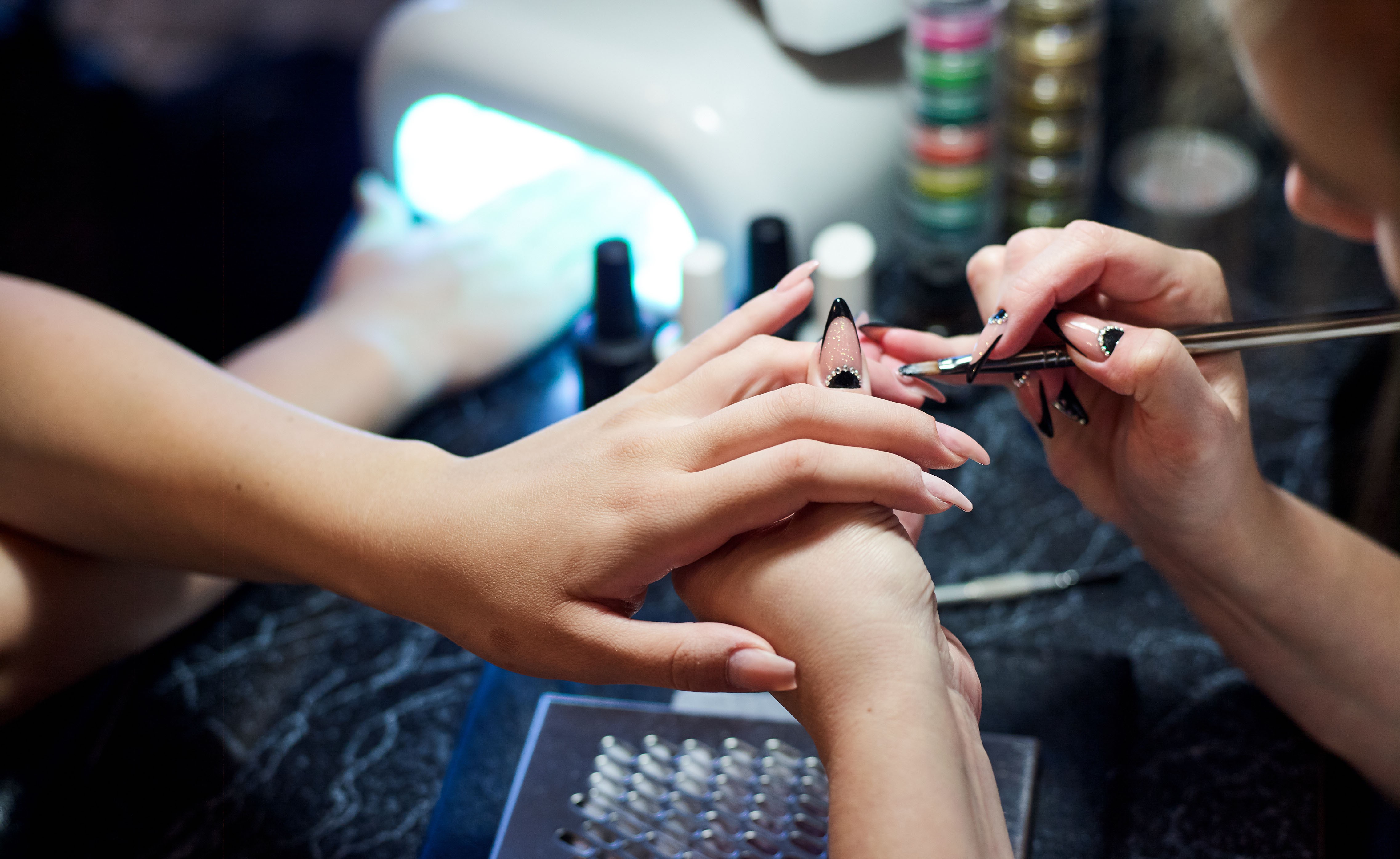 Nahaufnahme einer Frau im Nagelstudio, die von einer Kosmetikerin mit einer Nagelfeile eine Maniküre erhält.