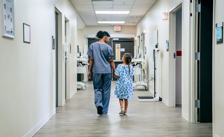 Pflegefachfrau läuft mit einem Mädchen einen Krankenhausflur entlang.