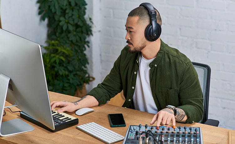 junger Mann arbeitet am PC mit Tontechnik und Kopfhörern